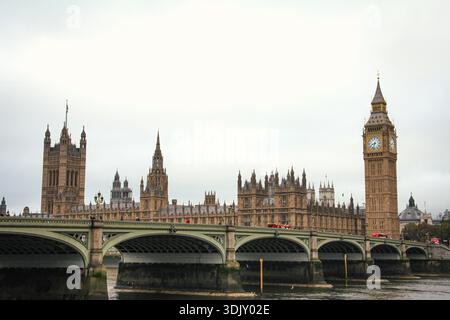 Der Palast von Westminster und der Big Ben Uhrenturm von der Themse aus gesehen mit Westminster Bridge und roten Bussen in London, Großbritannien. Stockfoto