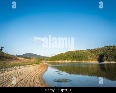 Ruhige Küste des Garasko jezero (Gardasee) in der Nähe von Arandjelovac, Serbien, mit einer Sandbank, Reflexionen auf stillen Wasser und bewaldeten Hügeln, eine malerische d Stockfoto