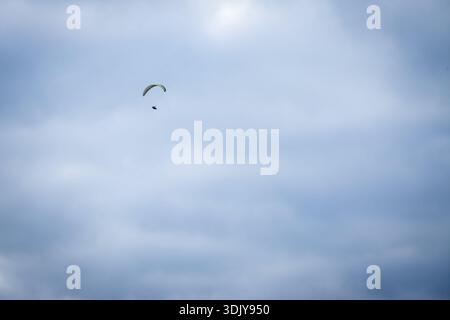 Ein einsamer Gleitschirmflieger mit einem bunten Flügel gleitet hoch gegen einen blassbewölkten Himmel und schafft eine minimalistische freie Flugszene mit großem Kopierraum und ruhigem A Stockfoto