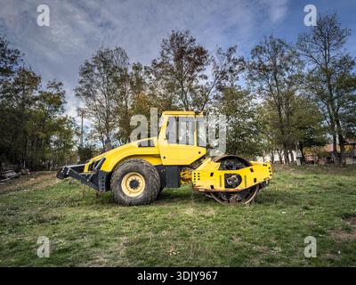 Gelbe Straßenwalze, kleines Modell, auf einer Wiese ausgestellt. Eine Straßenwalze oder Verdichterwalze wird für Asphalt und Straßenrenovierung und -Bau verwendet. Stockfoto