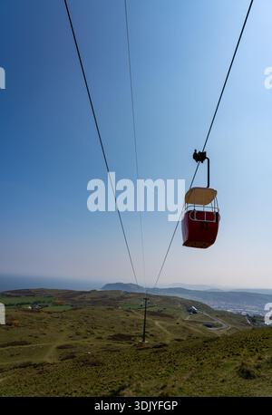 Rote Seilbahnkabine hängt an Stahlseilen über den grasbewachsenen Hängen der Great Orme Landzunge Stockfoto