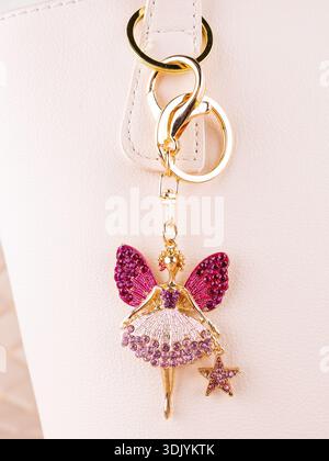 Nahaufnahme eines Schlüsselanhängers aus hellem Metall in Form einer Fee mit Flügeln aus rosa Strasssteinchen auf einer weißen Tasche Stockfoto