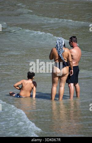 Paare mittleren Alters gehen Hand in Hand durch ruhiges Meerwasser und genießen Sonnenlicht Wärme und romantische Sommerverbindung. Stockfoto