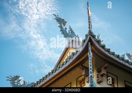 Drachenstatue auf dem Dach des thailändischen Tempels vor blauem Himmel, verzierte Drachenstatue krönt den buddhistischen Tempelgiebel Stockfoto