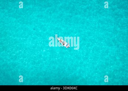 Aus der Vogelperspektive eines kleinen Bootes, das auf dem türkisfarbenen Wasser driftet, während die Sonne sich von den Wellen reflektiert und einen schimmernden Effekt erzeugt, Kalleesa, Jemen. Stockfoto