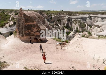Kappadokien, Türkei - 18. Mai 2025: Paare wandern in einem Sandtal in Kappadokien vorbei an Sattelpferden und warten auf Touren Stockfoto