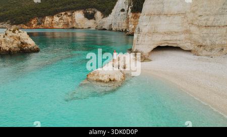Frau, die auf einem felsigen Vorsprung über einer klaren smaragdgrünen Bucht und weißen Klippen auf der Insel Kefalonia in Griechenland spaziert. Stockfoto