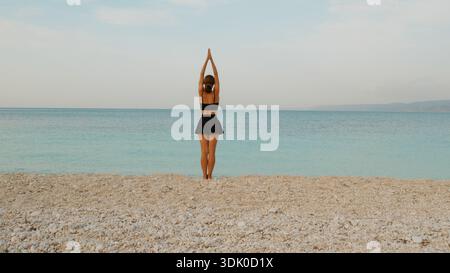 Frau mit Blick auf den Horizont, während sie an einem ruhigen Kiesstrand mit ruhigem türkisfarbenem Meer spaziert. Stockfoto