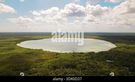 Kreisförmiger See umgeben von grünem Wald unter blauem Himmel in der Nähe von Tulum in Mexiko. Stockfoto