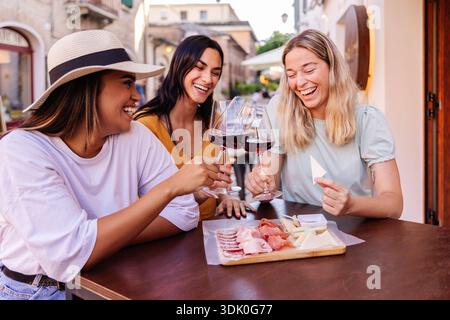 Junge multirassische Freundinnen trinken Wein in einem Café im Freien Stockfoto
