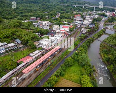 Aus der Vogelperspektive des Bahnhofs Shifen in Taiwan mit einem Zug auf den Gleisen, Menschen versammelten sich entlang der Eisenbahn und farbenfrohen Himmelslaternen, die darüber schweben. Stockfoto