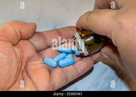 Mit der Hand blaue Pillen aus der Flasche in die Handfläche gießen Stockfoto