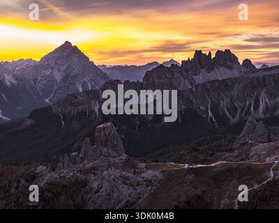 Aus der Vogelperspektive sehen Sie zerklüftete Berggipfel, die den goldenen Sonnenaufgang durchdringen und lange Schatten über das zerklüftete Gelände werfen, San Giovanni di Fassa, Trentino-Sout Stockfoto