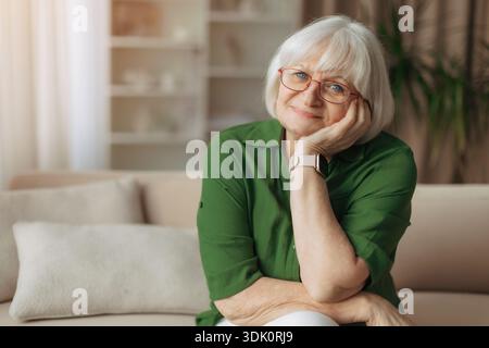 Ältere kaukasische Frau, die Kopf auf der Hand liegt und sanft zu Hause lächelt Stockfoto