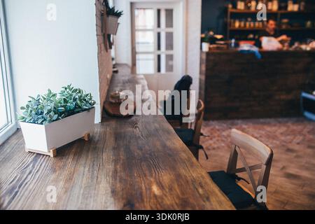 Einladende rustikale Kaffee- und Pflanzenstation. Warme Holztheke mit üppig grünen Topfpflanzen. Charmanter rustikaler Kaffeespot mit Holzoberfläche und Stockfoto