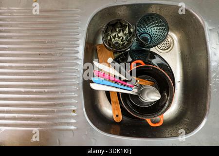 Schmutziges Geschirr und Küchenutensilien stapelbar in einem Edelstahlbecken nach dem Kochen. Alltägliches Haushaltskonzept, Haushaltsarbeiten, Reinigungsroutine Stockfoto