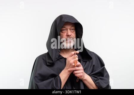 Ein älterer Mönch in schwarzem Gewand hält den Rosenkranz und blickt zur Seite Stockfoto