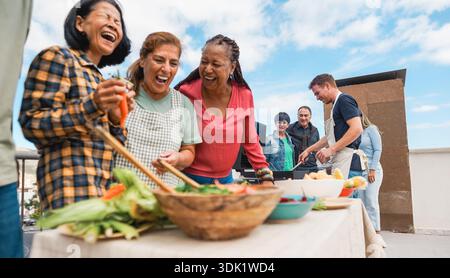 Menschen mit mehreren Generationen, die auf dem Dach des Hauses grillen - Freunde mit mehreren Rassen, die am Wochenende Spaß beim Essen und Kochen haben - Sommer und Essen Stockfoto