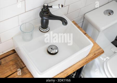 Modernes Badezimmer mit weißen U-Bahn-Fliesen, quadratischem Keramikwaschbecken und schwarzem Armatur im Vintage-Stil mit weißen Keramikdetails Stockfoto