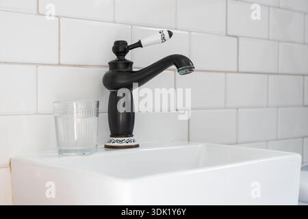 Modernes Badezimmer mit weißen U-Bahn-Fliesen, quadratischem Keramikwaschbecken und schwarzem Armatur im Vintage-Stil mit weißen Keramikdetails Stockfoto