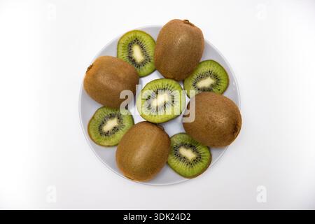 Frische Kiwis auf Teller auf weißem Hintergrund, Draufsicht mit Kopierraum Stockfoto