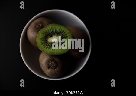 Kiwi Frucht halb in Schüssel auf schwarzem Hintergrund, Draufsicht Stockfoto