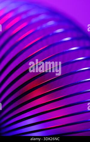 Nahaufnahme einer Spiralfeder mit ausreichend hohen Festigkeit und elastischen Eigenschaften in Neonviolett und rosa Licht. Makrofoto, selektiver Fokus. Stockfoto