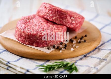 Rohe gehackte Rindfleischpasteten für Burger auf einem weißen Tisch. Zwei frische, rohe Hamburger-Patties auf einem weißen Tisch. Frisch gemahlene Rindfleisch-Burger-Patties mit Salz Stockfoto
