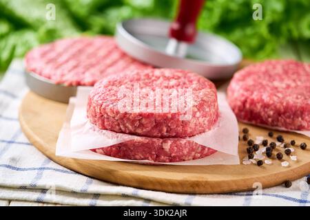 Stapel roher Burger-Rindfleisch-Patties auf einem weißen Tisch, selektiv fokussiert. Natürliches Fleischprodukt. Uniform-Patties kochen in der Burgerpresse. Stockfoto