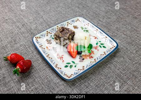 Eine Nahaufnahme eines eleganten Desserttellers mit einem Stück reichhaltigen Schokoladenkuchen (Brownie), einer Schaufel Vanilleeis und einer ganzen, in Scheiben geschnittenen frischen Stra Stockfoto