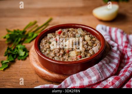 Hausgemachte Linsensuppe und Eintopf im Topf nah auf Holztisch mit Tischtuch Stockfoto