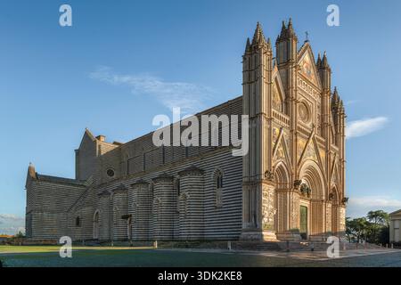 Außenansicht der Kathedrale von Orvieto, Duomo di Orvieto, bei Sonnenuntergang. Gotische Fassade mit goldenen Mosaiken und gestreiften Marmorwänden, Region Umbrien, Italien Stockfoto