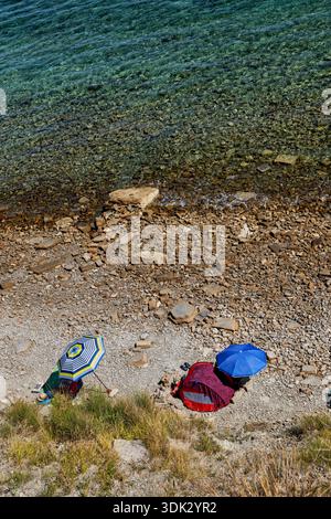 Blick über den Kiesstrand mit Menschen unter Sonnenschirmen und Zelt an der Adria in Piran, Slowenien. Stockfoto