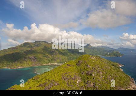 Aus der Vogelperspektive auf die grünen Hügel treffen auf das türkisfarbene Wasser, unter einem Wolkenhimmel, auf die Seychellen, auf die Seychellen. Stockfoto