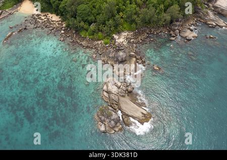 Blick aus der Vogelperspektive auf das türkisfarbene Wasser mit zerklüfteten Felsvorsprüngen und grünen tropischen Blättern, Seychellen und Seychellen. Stockfoto