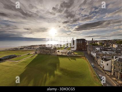 Blick aus der Vogelperspektive auf das goldene Sonnenlicht, das das gepflegte Grün des Golfplatzes küsst und auf die zerklüftete Küste und die historischen Gebäude St. Andrews, SCO trifft Stockfoto