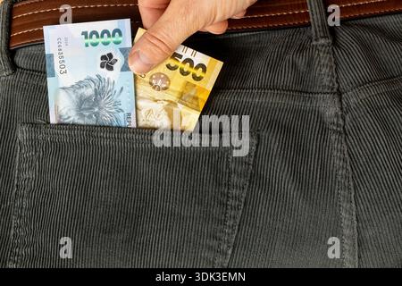 Philippinischer Peso. Eine Hand, die gegen Geld in die Hosentasche greift. Banknoten in Höhe von 1.500 philippinischen Pesos Stockfoto