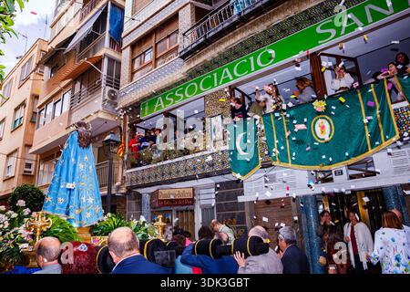 Eine Nahaufnahme des Wasserwagens der Jungfrau Maria, während er unter einem Balkon mit Leuten vorbeigeht, die bunte Papiere (Aleluyas) werfen. Die Menge unter c Stockfoto