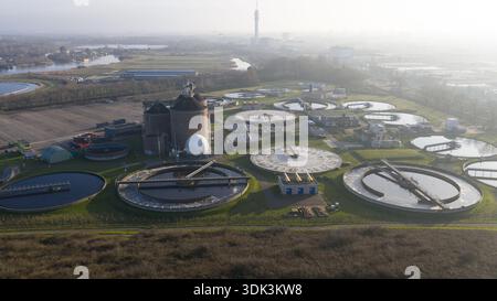 Aus der Vogelperspektive der kreisförmigen Wasseraufbereitungsbecken, die den Himmel reflektieren, neben zylindrischen Strukturen, die vor einem trüben Horizont stehen, Abwasserbehandlung Stockfoto