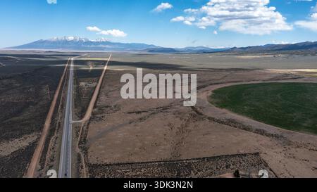 Blick auf ein langes Autobahnband, das sich über die trockene Landschaft in Richtung entfernter schneebedeckter Berge unter einem riesigen blauen Himmel erstreckt, Winslow, Arizona, U Stockfoto