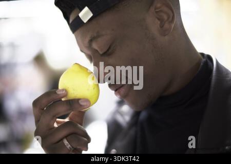 Afrikanischer Mann hält und riecht eine Zitrone, gelbe Zitrusfrucht, sieht nachdenklich in einem Nahaufnahme, Achtsamkeit, gesunde Ernährung, Vitamin C, Stren Stockfoto