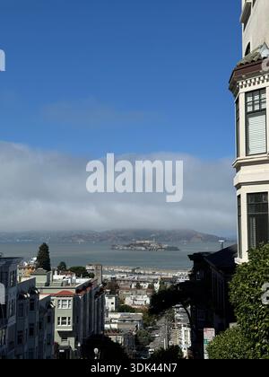 Blick auf Alcatraz Island über die Bucht von San Francisco, eingerahmt von Wohnhäusern an einer steilen Stadtstraße. Stockfoto