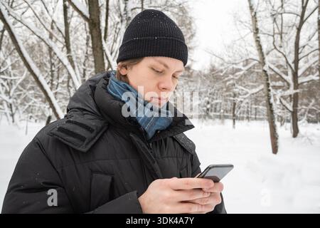 Junger Mann mit Smartphone im verschneiten Wald Stockfoto