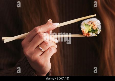 Frau, die Sushi-Rolle mit Stäbchen in der Nähe hält. Japanische Küche und gesundes asiatisches Essenskonzept während der Mahlzeit im Restaurant. Stockfoto