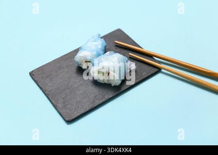 Leckere Sushi-Brötchen mit Kunststoff auf Teller vor blauem Hintergrund. Mikroplastik-Bewusstseinsmonat Stockfoto