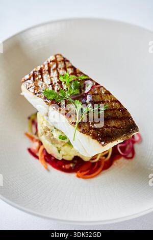 Gegrilltes Wolfsbarschfilet auf einem Bett aus Kartoffeln und Gemüse Stockfoto