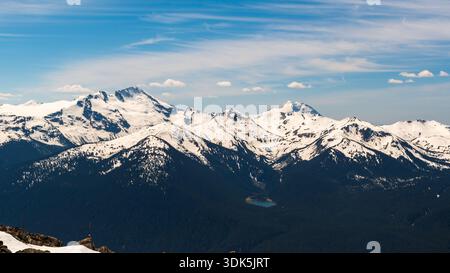 Whistler, BC, Kanada - 21. Juni 2024: Schneebedeckte Gipfel mit einem Bergsee an der Basis erstrecken sich über die Distanz vom Top of the World Summit. Stockfoto