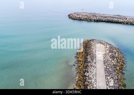 Aus der Vogelperspektive auf einen Hafeneingang mit zwei Steinbruchbrechern und einem kleinen Leuchtturm auf einem ruhigen Meer Stockfoto