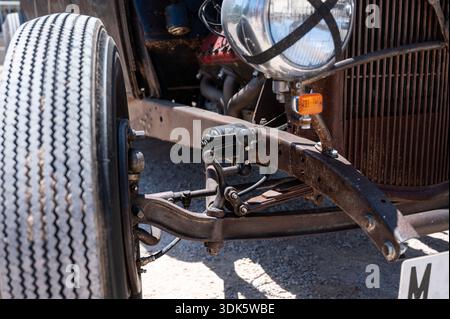Eine detaillierte Nahaufnahme der rostigen Vorderradaufhängung eines 1932 Ford Rat Rod mit klassischer Vollachsachse, Blattfedern und Lenkungskomponenten Stockfoto