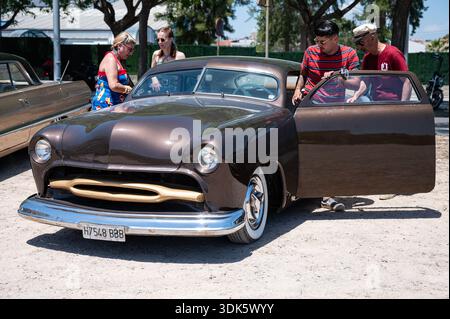 Ein maßgeschneiderter 1949er Ford Mercury Shoebox Hot Rod in Braun mit abgesenktem Dach und offener Tür, mit Freunden, die bei einem Oldtimer-Event in das Auto steigen. Stockfoto